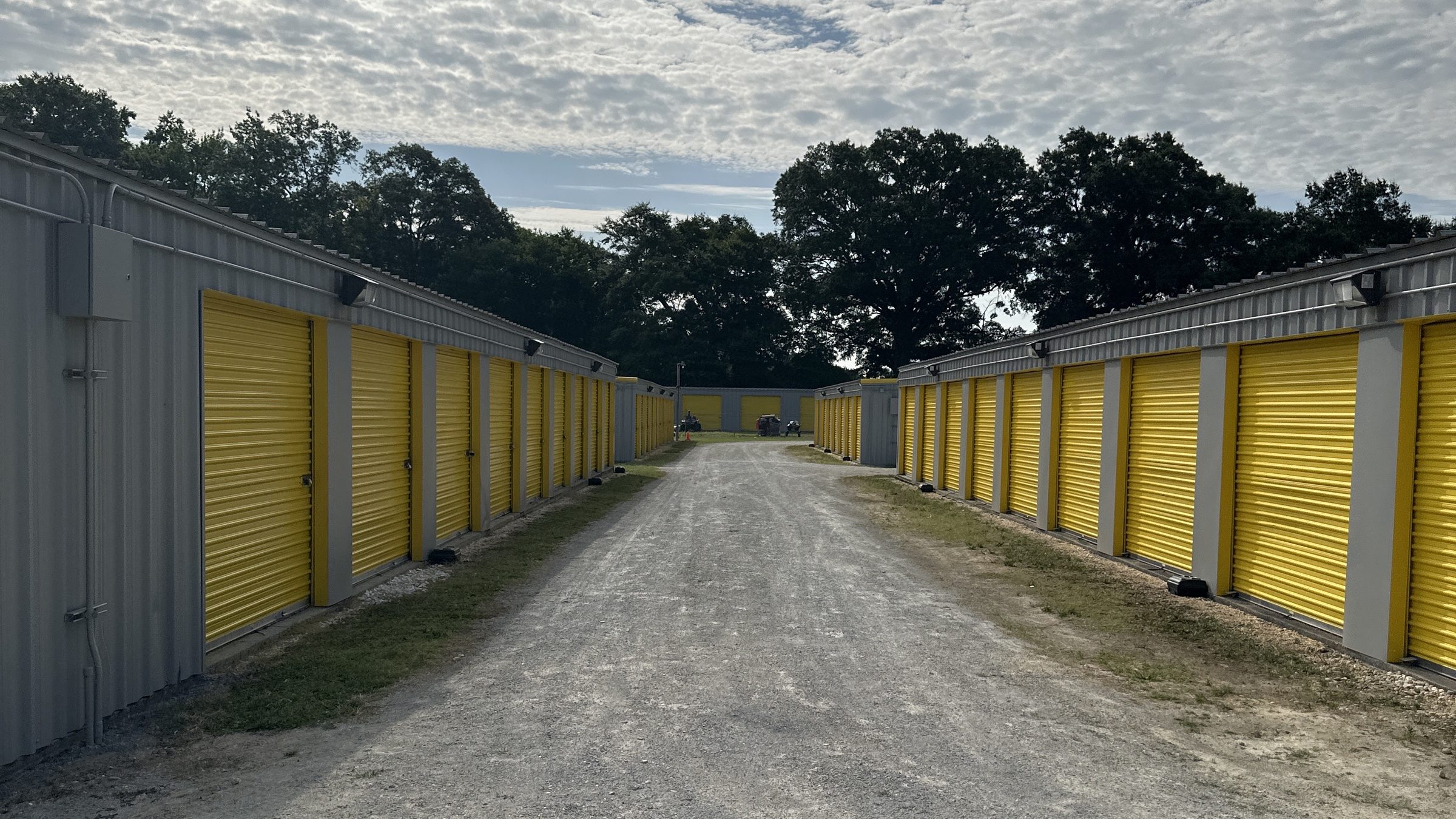 Gravel drive aisle between rows of yellow roll-up doors at Self Storage Goldsboro